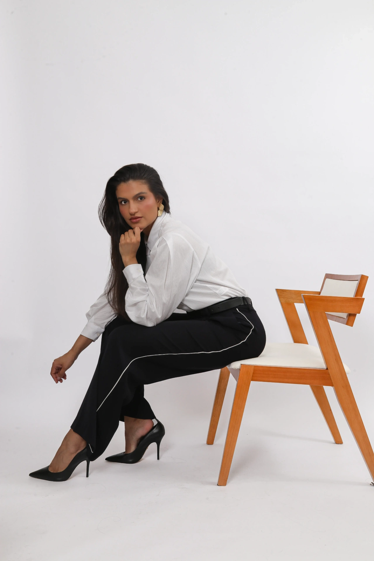 Amanda Siara sentada de perfil em cadeira de madeira com mão no rosto