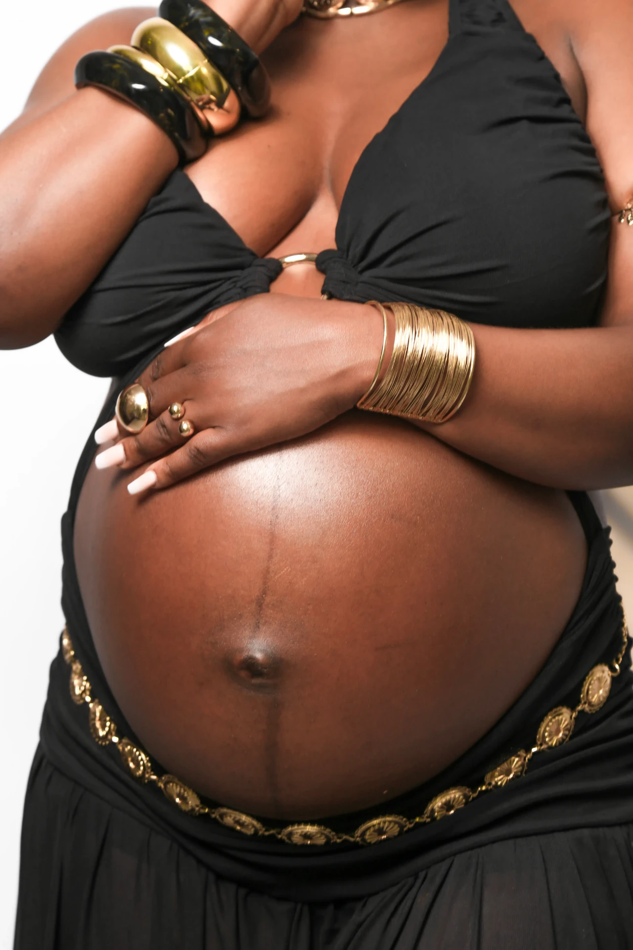 Detalhe da barriga da gestante com cinto e braceletes dourados
