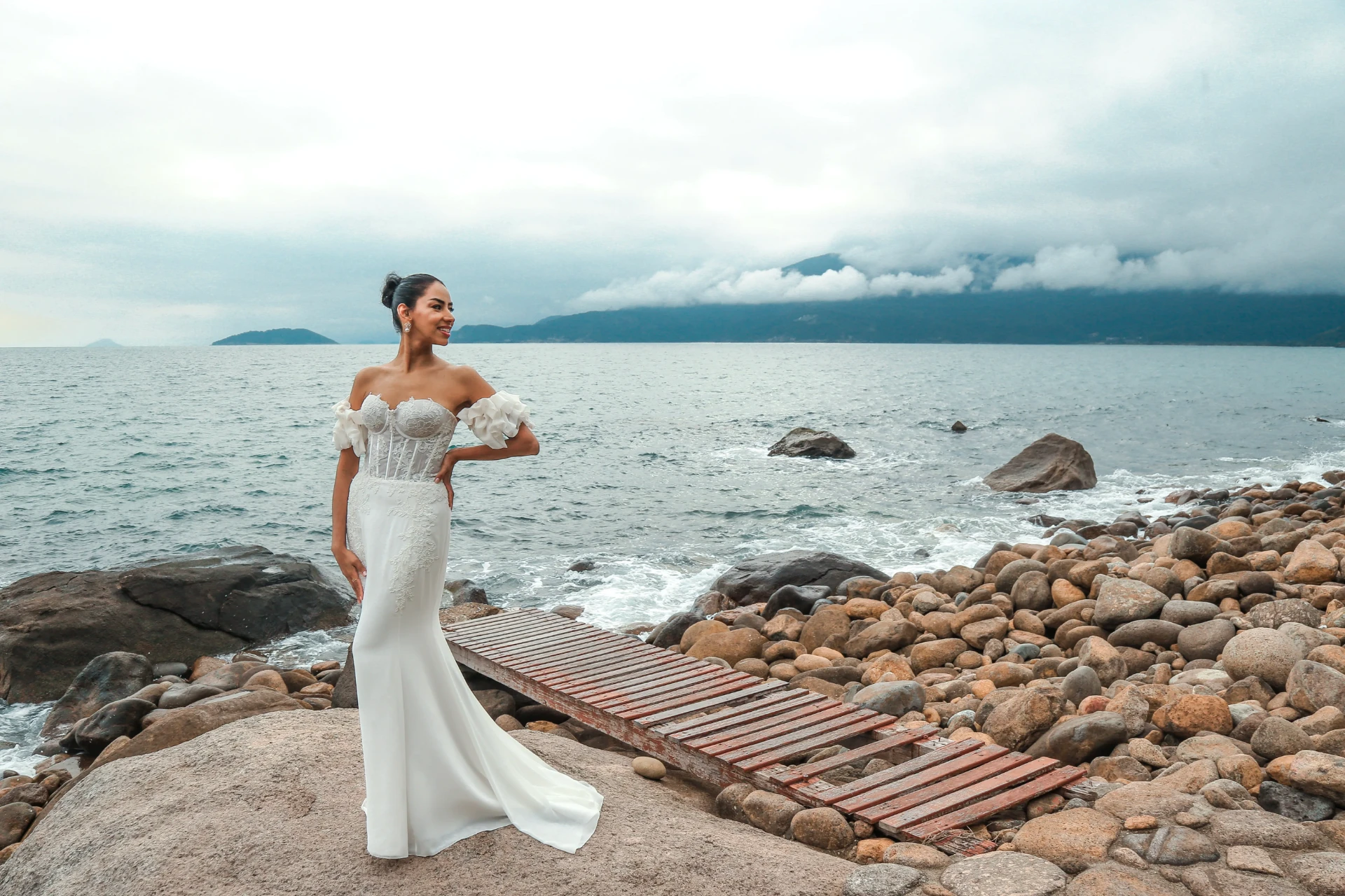 Larissa e Roberto — noiva de corpo inteiro na pedra com o mar e a serra ao fundo