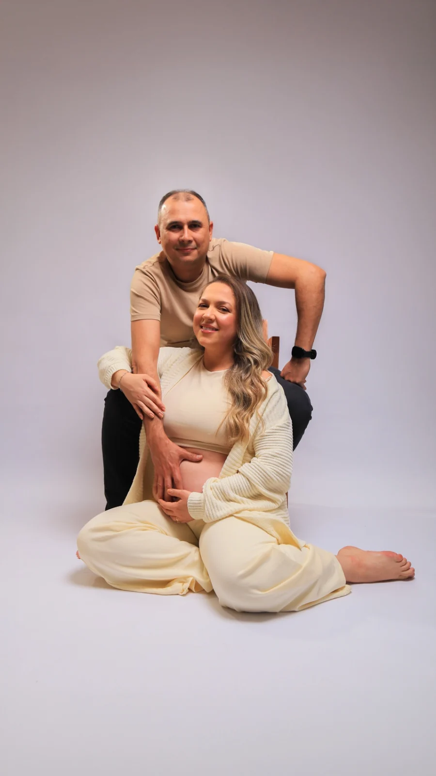Deborah sentada com Wellington atrás em fundo claro