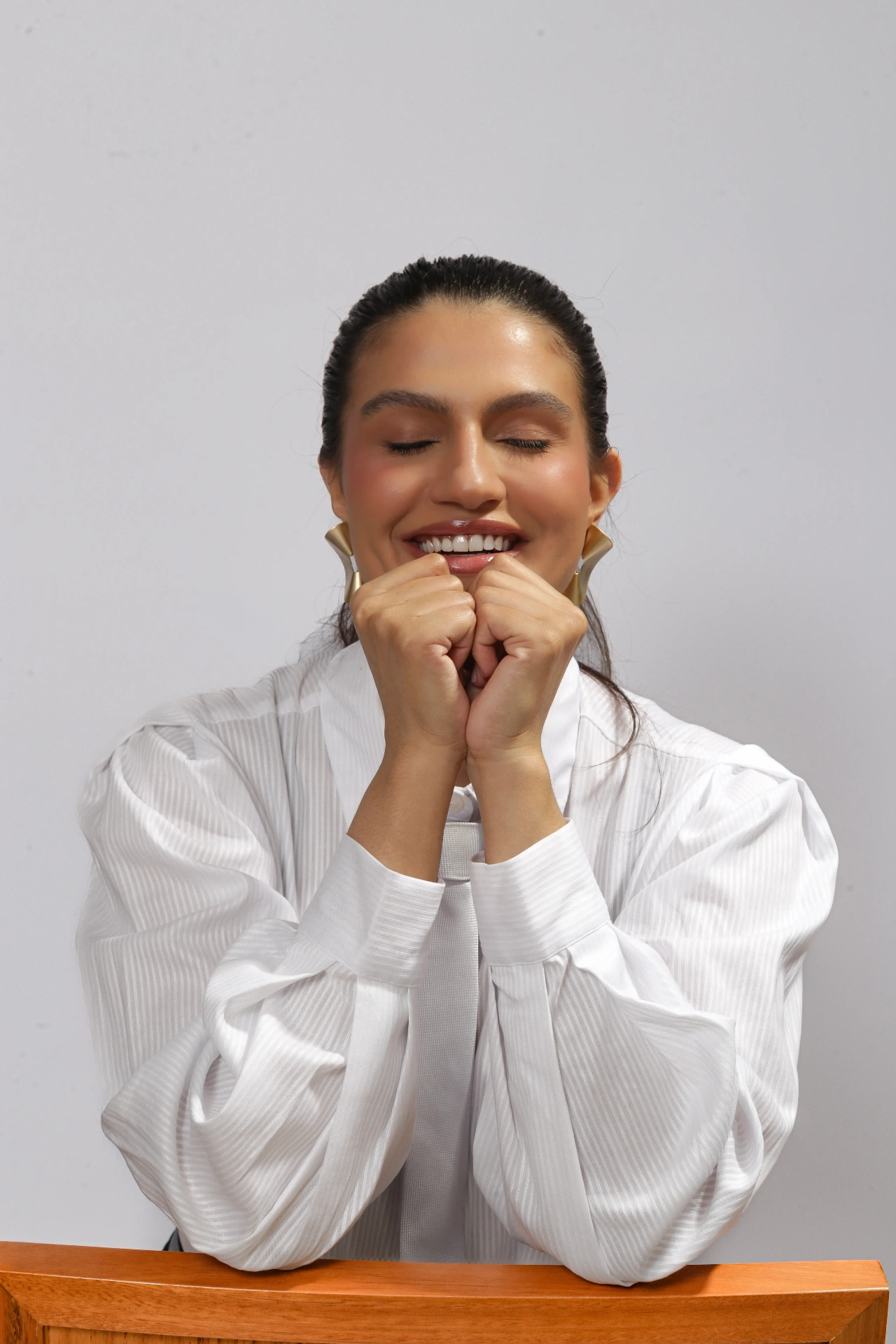 Amanda Siara sorrindo com os olhos fechados e mãos no queixo