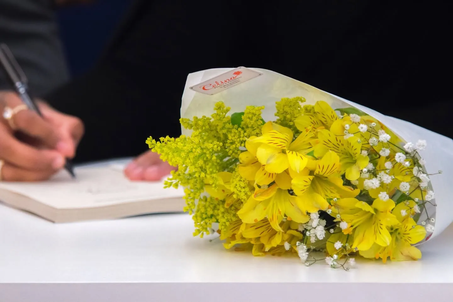 Lançamento do livro O Preço da Alma — buquê de flores amarelas e mão autografando livro