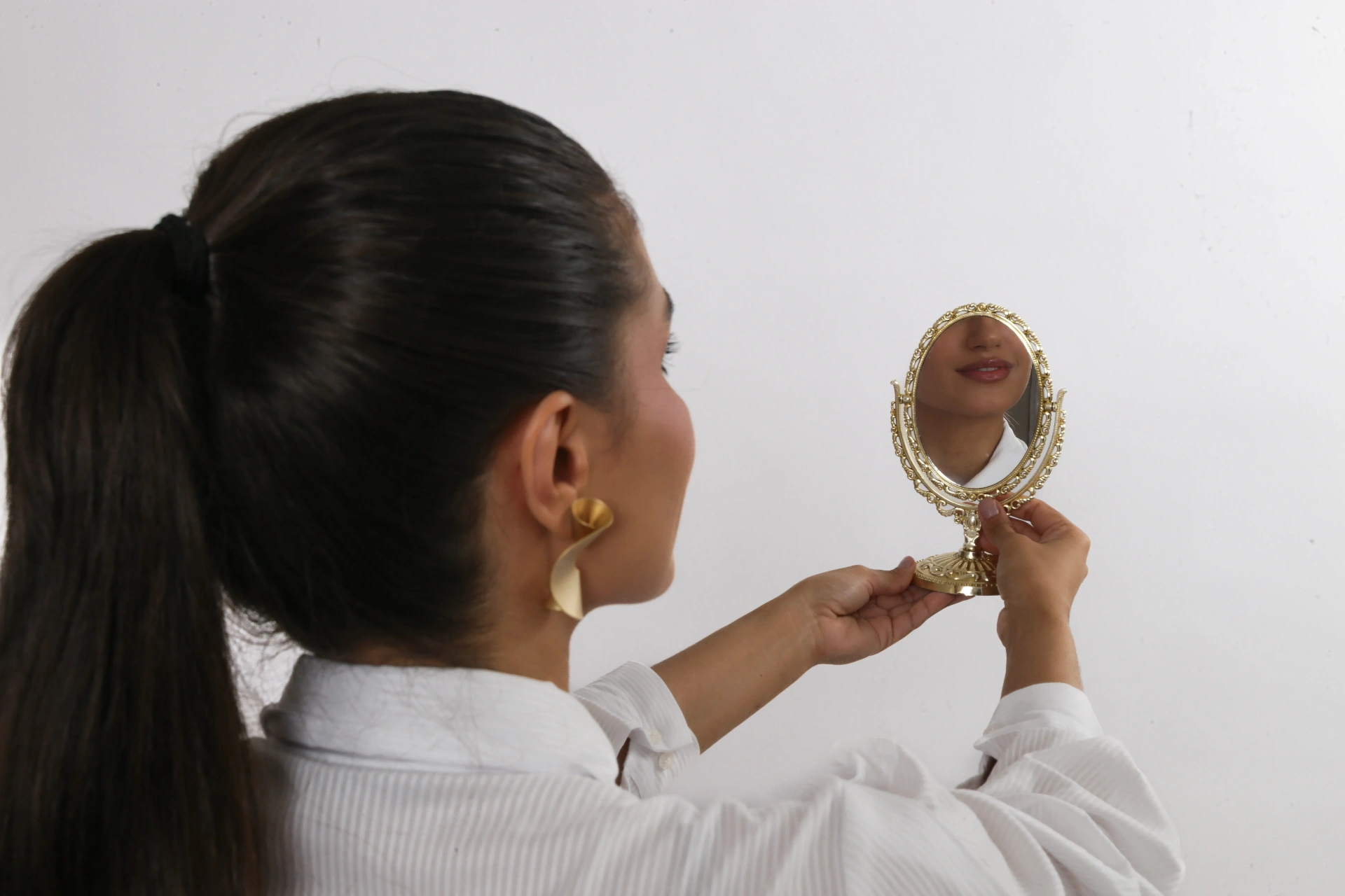 Amanda Siara de costas segurando espelho dourado refletindo o sorriso