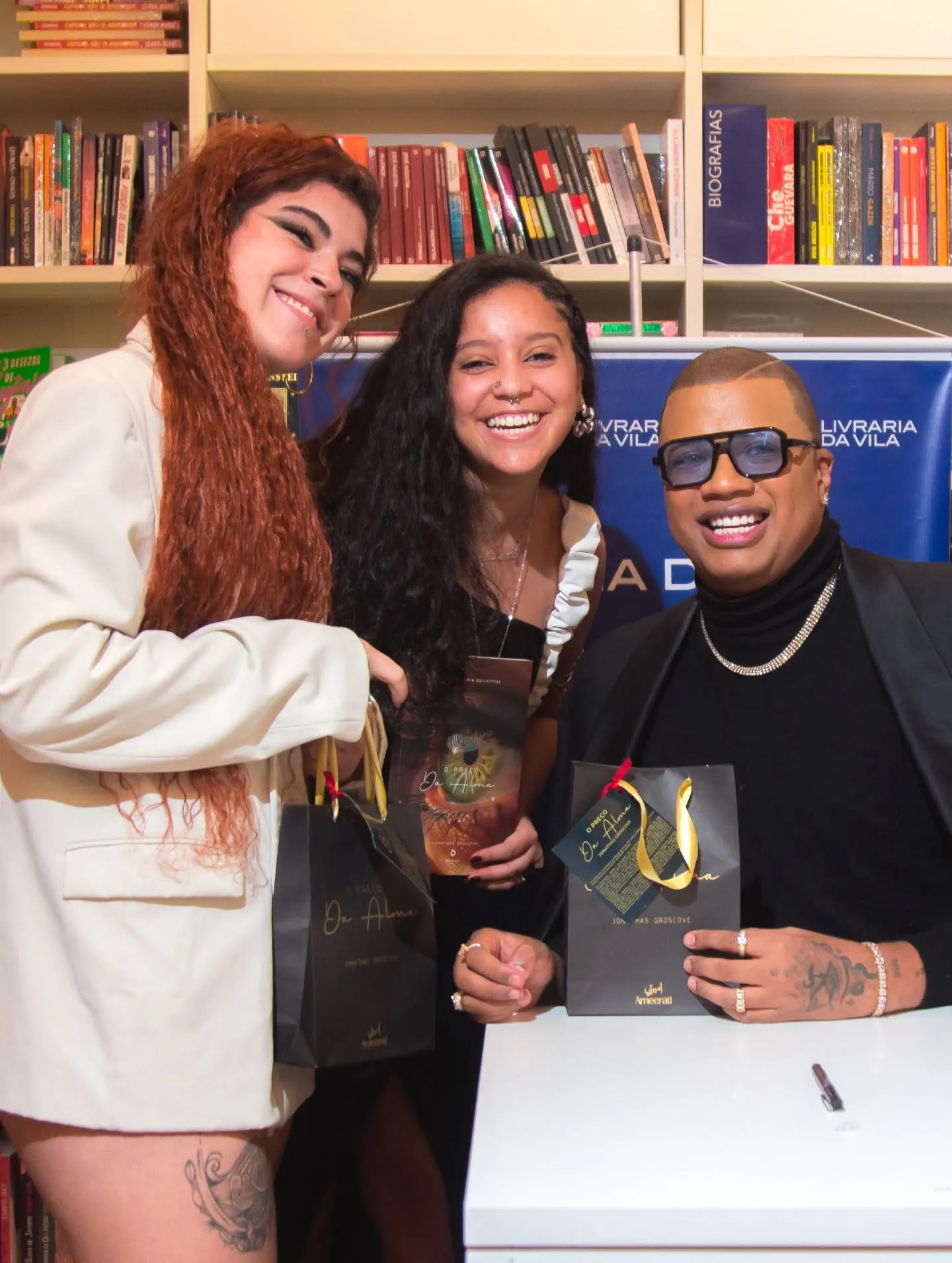 Lançamento do livro O Preço da Alma — autor com duas convidadas segurando sacolas do livro