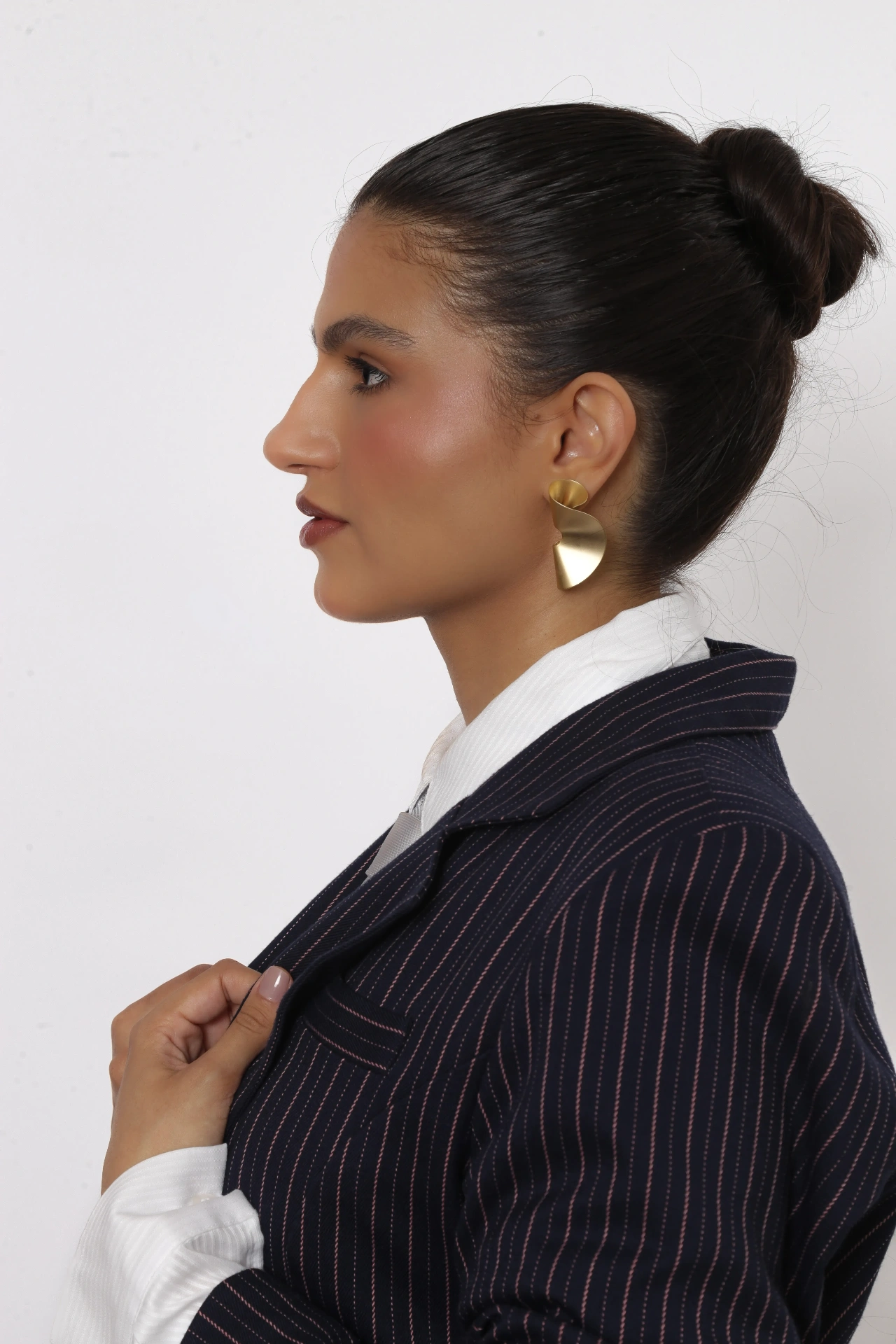 Amanda Siara perfil em close com brinco dourado e blazer risca de giz
