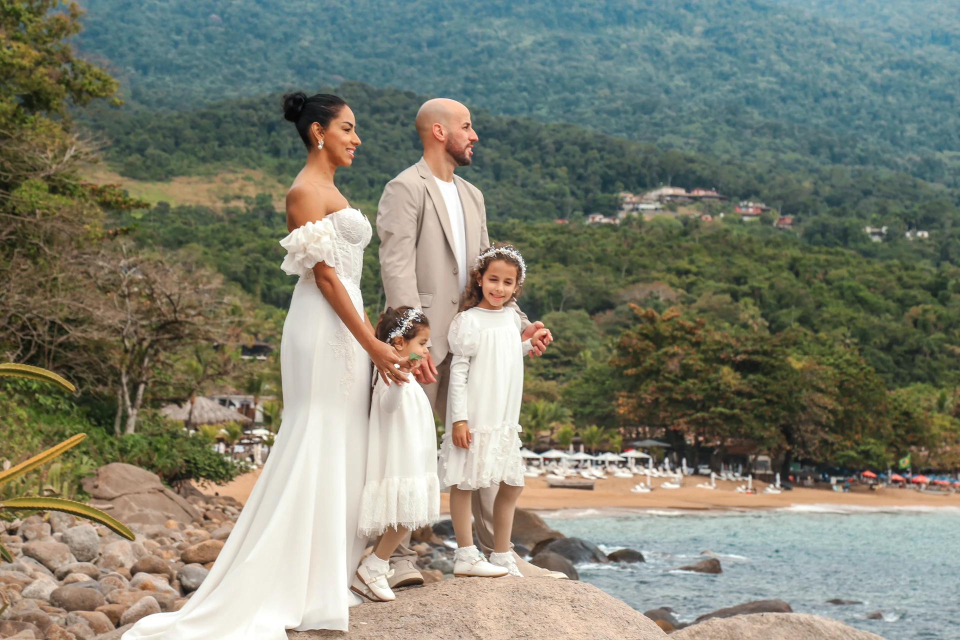 Larissa e Roberto — noivos e as duas daminhas na pedra com vista para a praia