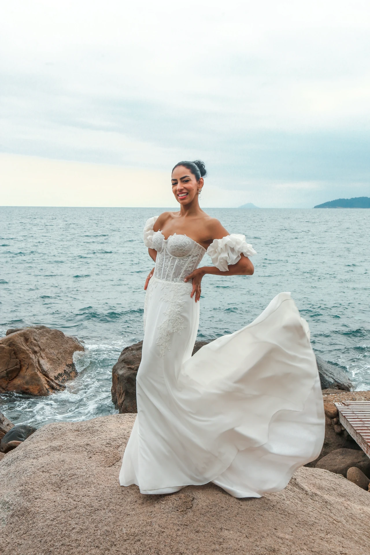 Larissa e Roberto — noiva com o vestido esvoaçante sobre a pedra à beira-mar
