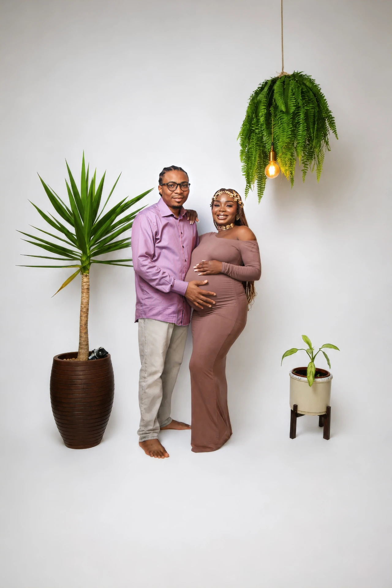 Casal gestante ao lado de plantas e luminária no estúdio