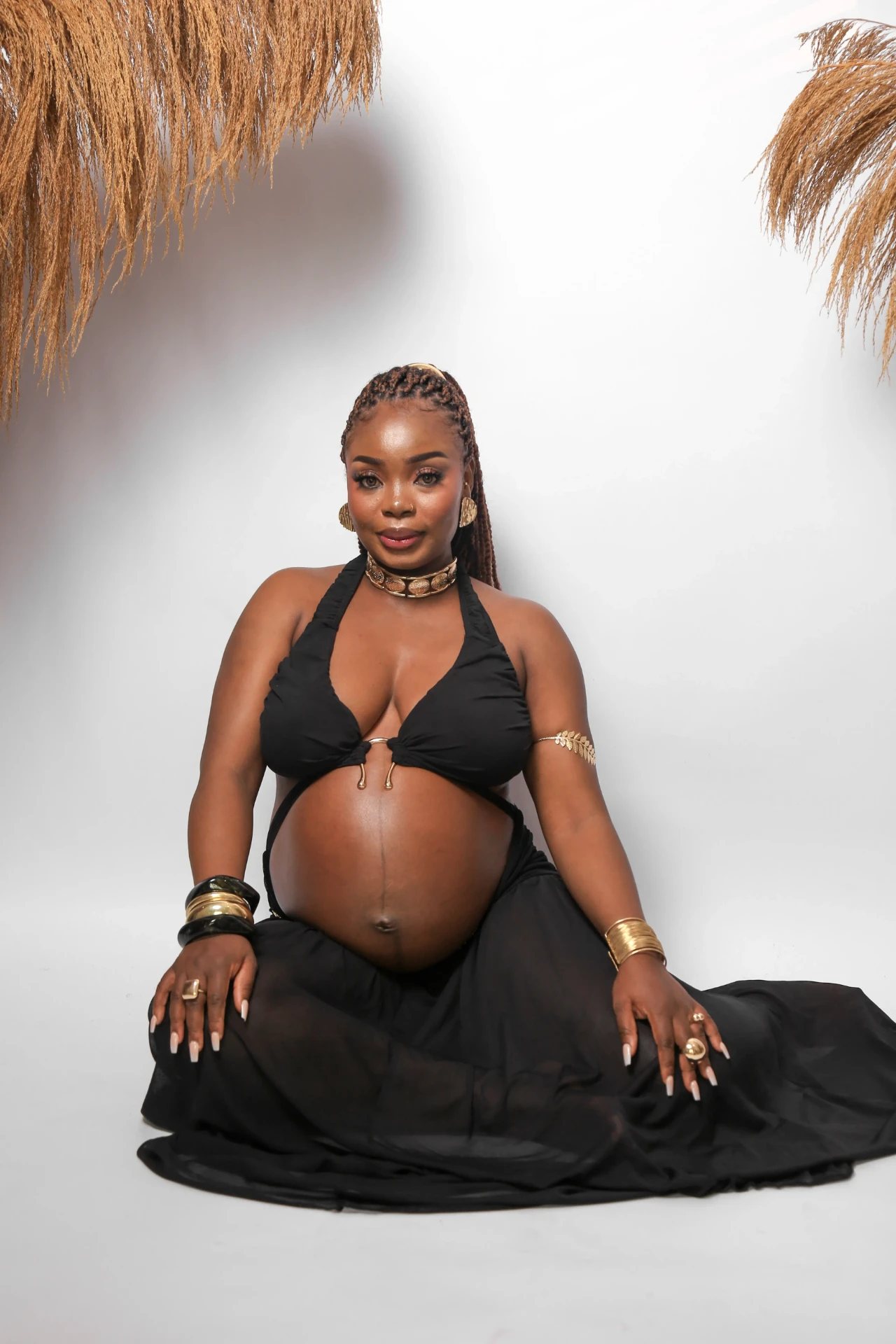 Gladys Ojonugwa gestante sentada com adornos dourados
