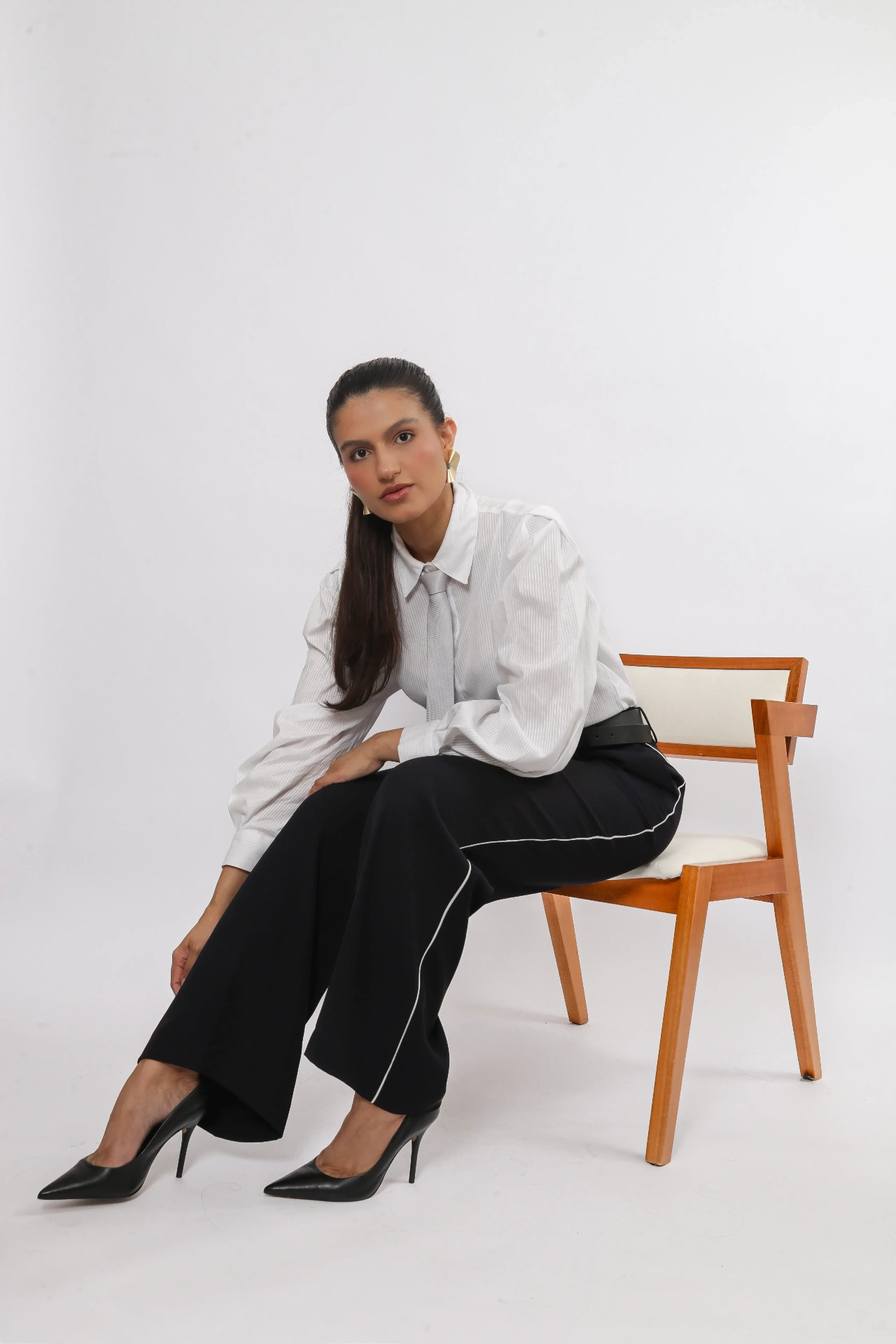 Amanda Siara sentada em cadeira de madeira com camisa branca e calça preta