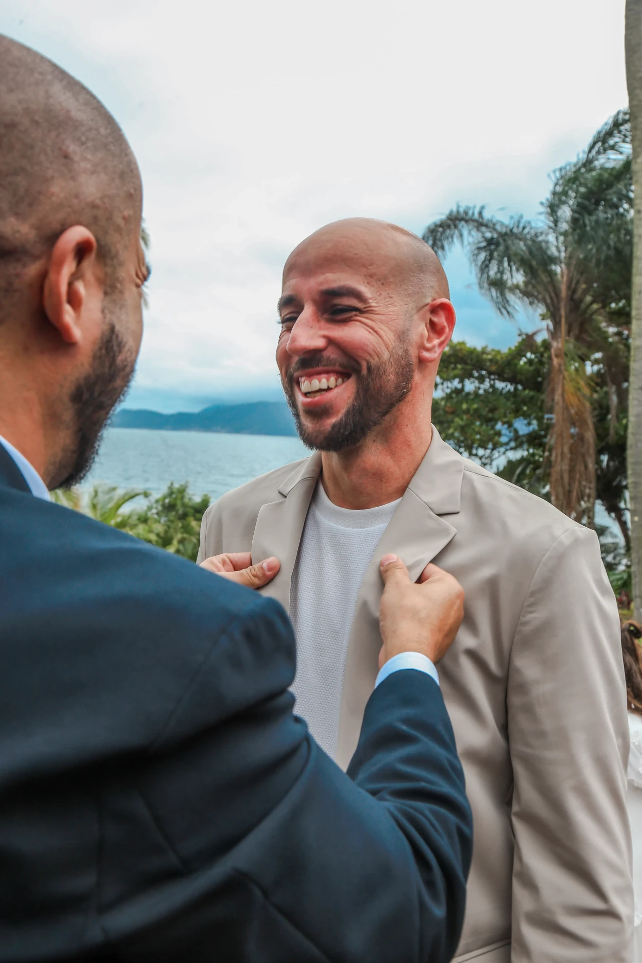 Larissa e Roberto — padrinho ajustando o blazer do noivo à beira-mar