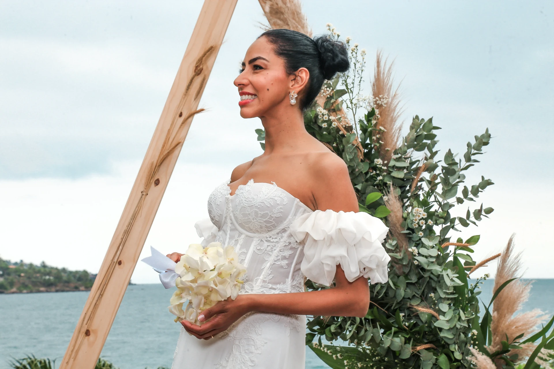 Larissa e Roberto — noiva de perfil sorrindo diante do arranjo de eucalipto