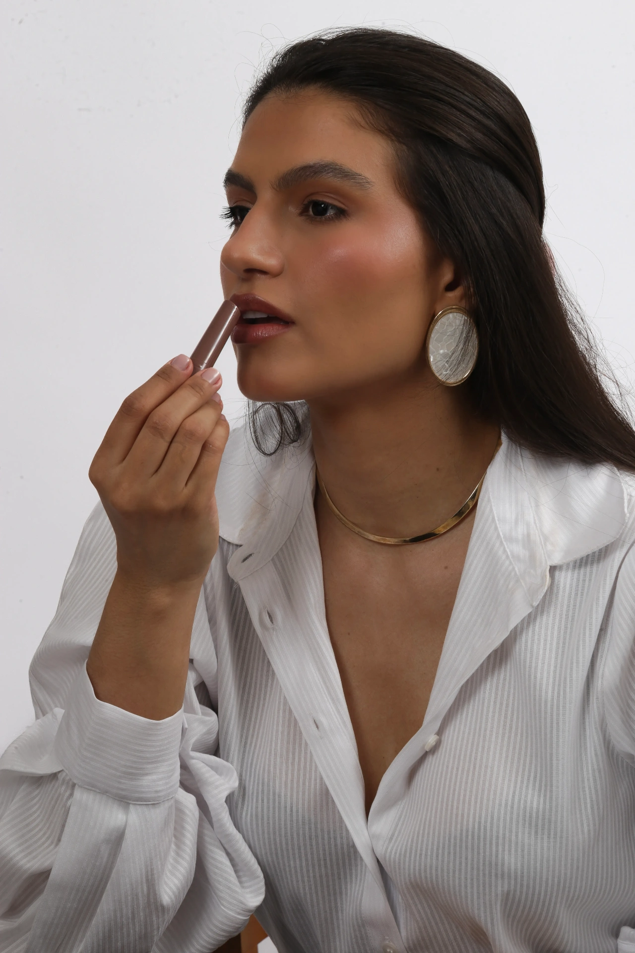 Amanda Siara passando batom com colar dourado e brinco oval