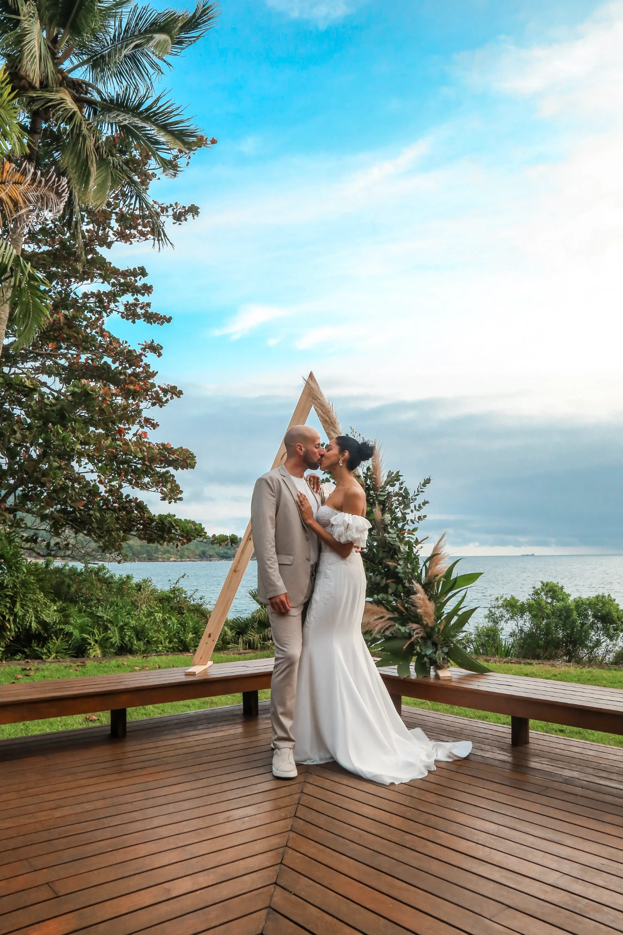 Larissa e Roberto — noivos se beijando sob o altar triangular à beira-mar