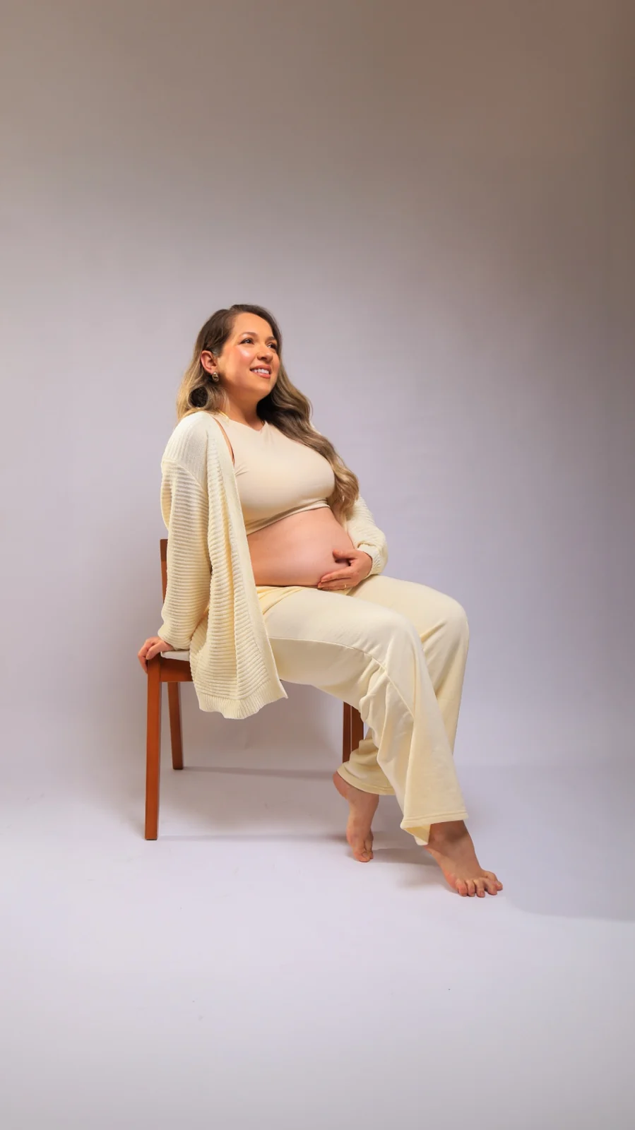 Deborah gestante sentada em cadeira com roupa clara